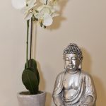 A silver buddha sitting on a table next to a white lily